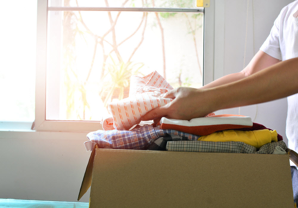 Person folding clothes and placing them in a donations box. 