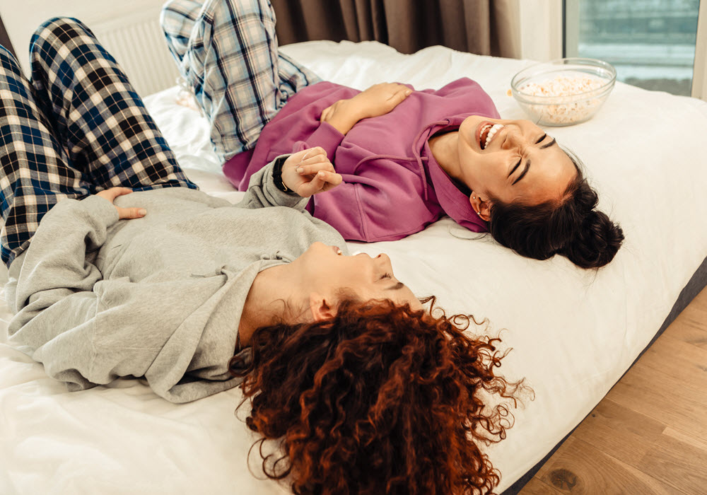 Roommates laughing while lying on bed. 