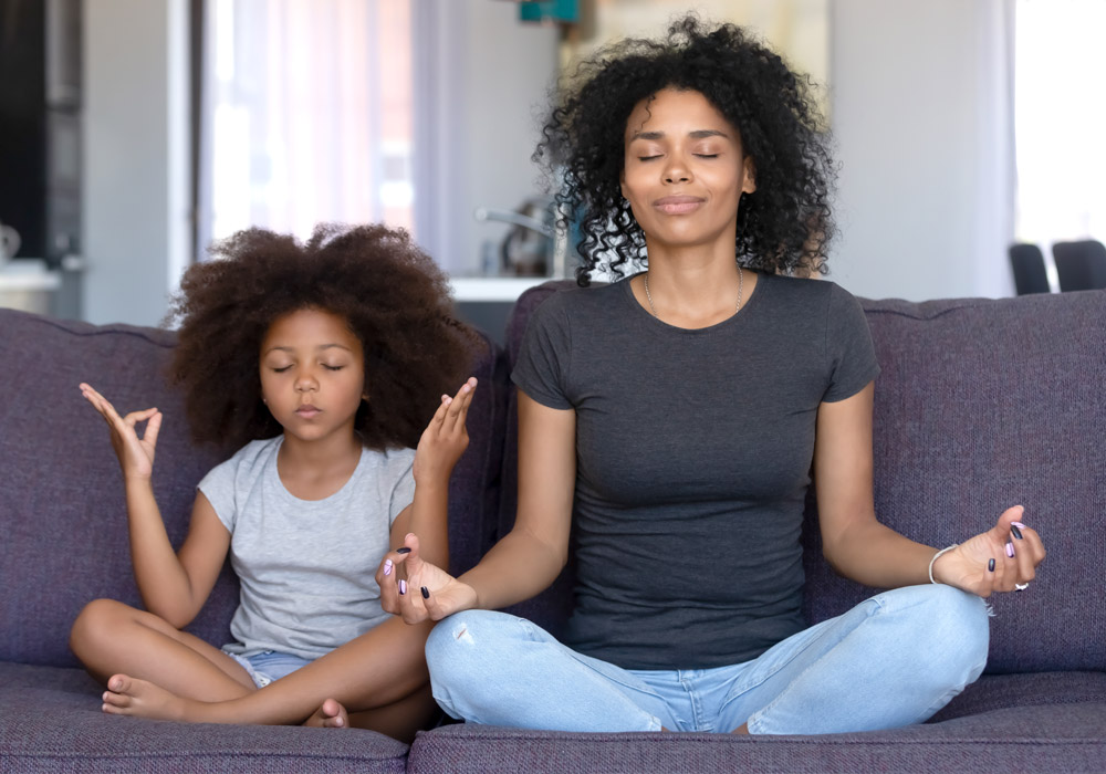 Mother and daughter meditating together at home in apartment living room