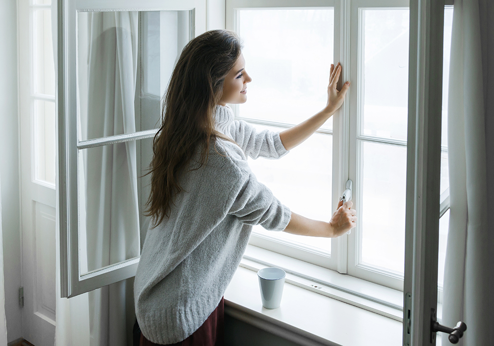 Woman in sweater closing window in her apartment