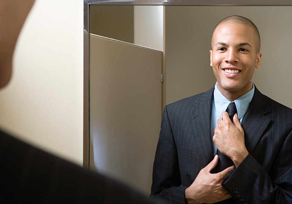Man fixing tie in bathroom mirror