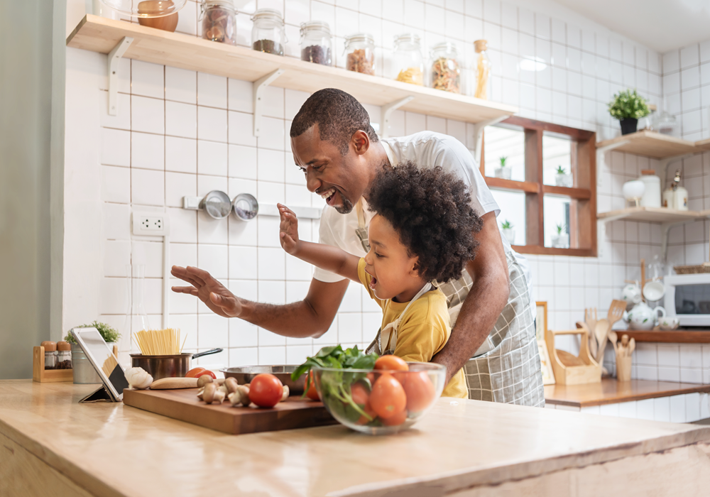 Man and son keeping their spirits high by making a video call while cooking in their apartment home.