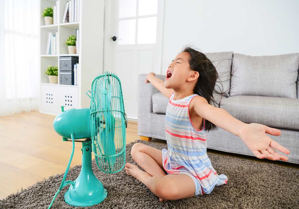Girl sitting with open arms in front of oscillating fan.