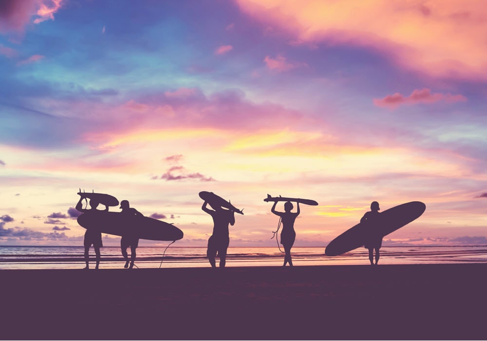 Silhouette's of surfers walking on the beach carrying their surfboards to the ocean