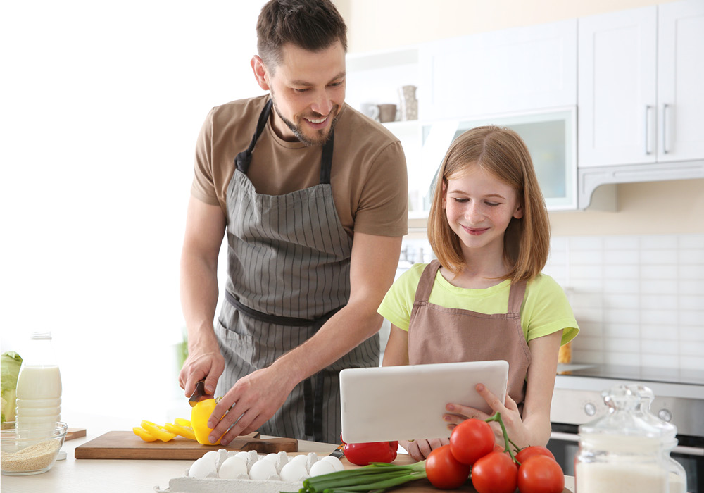 Father and daughter learning online with a tablet while cooking together