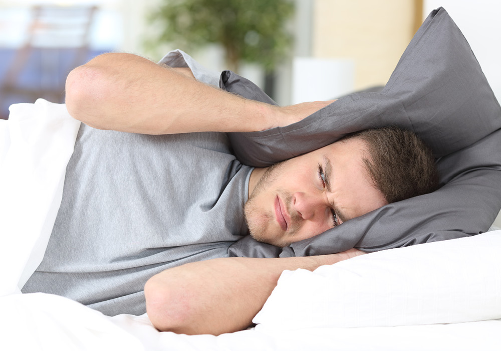 Man blocking out noise with his pillow to ears.