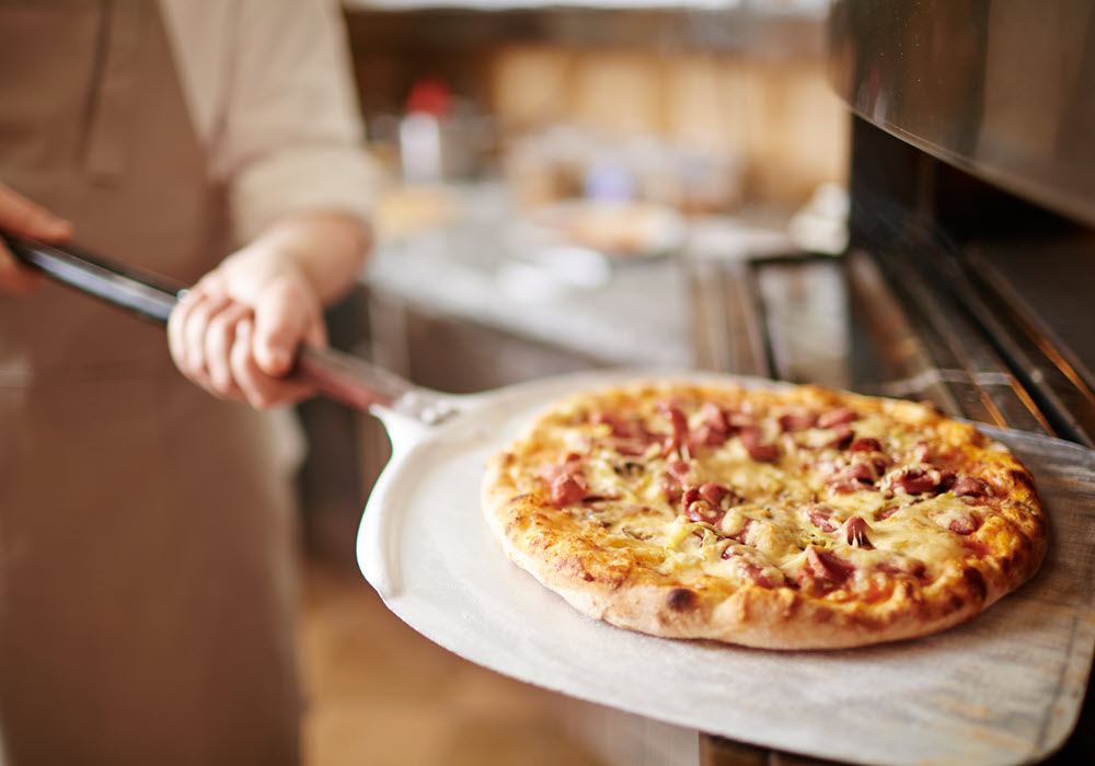 Pizza getting transferred into oven.