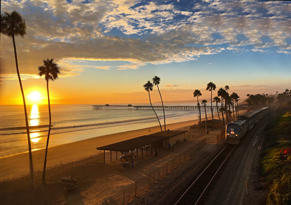 Beach with palm trees and train tracks at sunset.