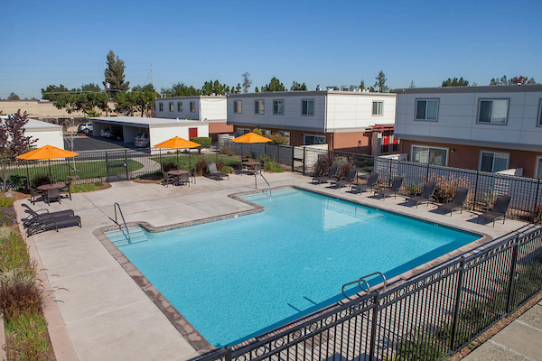 Gated outdoor swimming pool with sundeck and lounge seating.