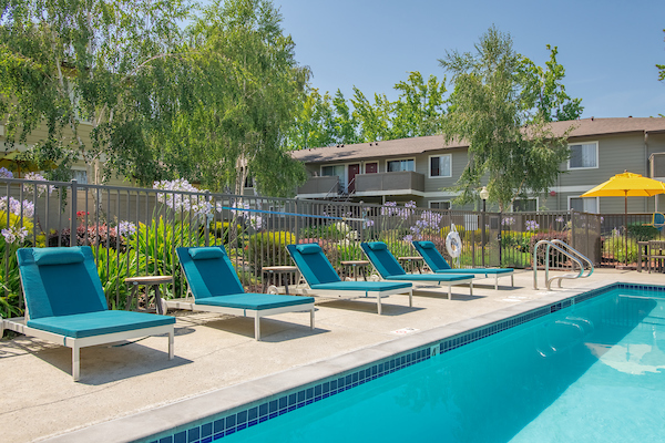 Outdoor swimming pool area with lounge seating surrounded by lush landscaping.